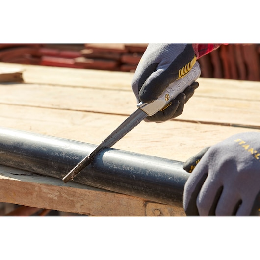 Photo of STANLEY 0-10-129 utility knife cutting a black plastic pipe, worker with gloves in outdoor setting.