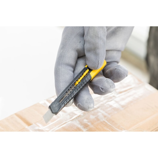 STANLEY 0-10-150 utility knife with grey gloves cutting tape on a cardboard box, close-up photography.