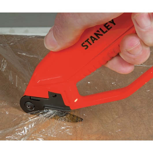 STANLEY 0-10-244 safety knife cutting plastic wrap on cardboard, close-up view.