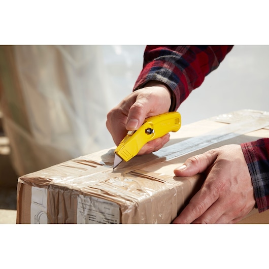 STANLEY 0-10-707 yellow utility knife cutting packaging tape on a cardboard box, close-up action view.