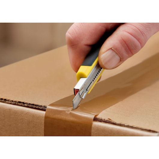 STANLEY 0-11-300 utility knife cutting brown tape on cardboard box, close-up photography.