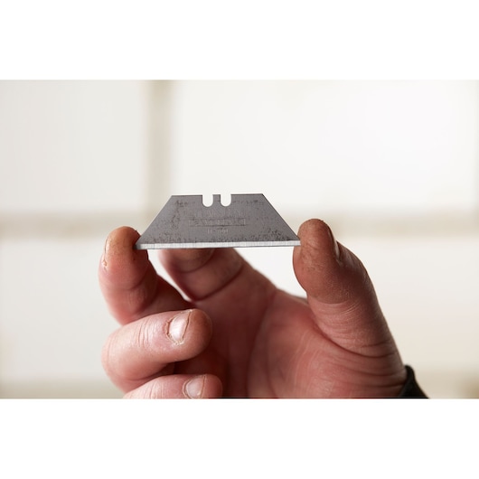 Photo of STANLEY 0-11-700 utility knife blade held between fingers, showing sharp edge and notched design.
