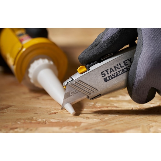Photo of STANLEY 0-11-800 utility knife cutting a caulk tube tip, close-up on wooden surface.
