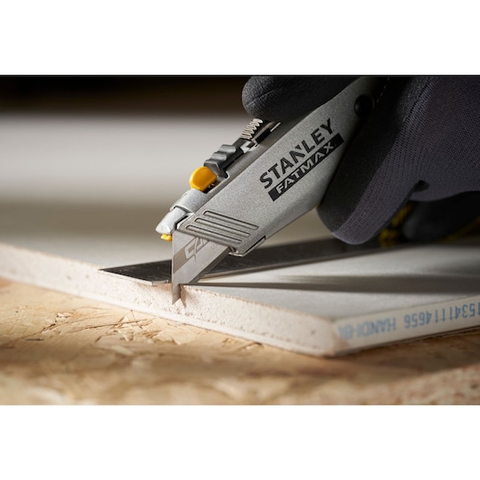 Photo of STANLEY 0-11-800 utility knife cutting drywall, close-up of blade and silver handle.