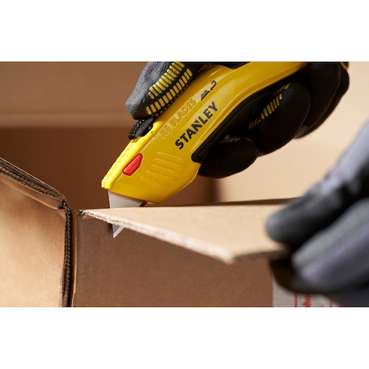 STANLEY 0-11-921 utility knife cutting cardboard, close-up, yellow handle, gloved hand.