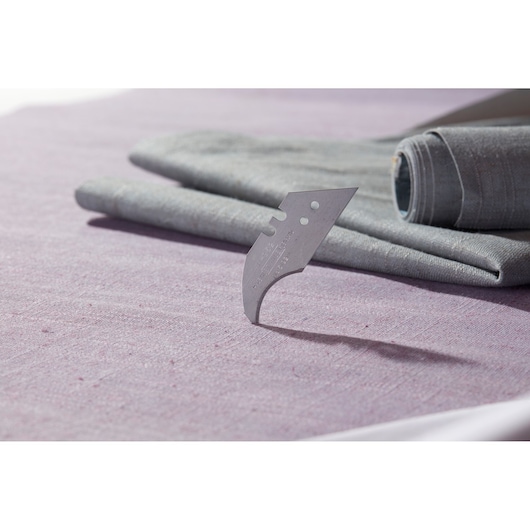 STANLEY 0-11-952 curved utility blade on purple fabric, two grey rolled textiles in background.