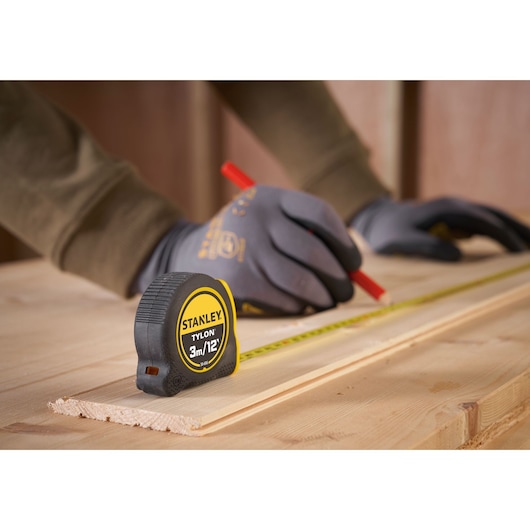 STANLEY 0-30-686 tape measure on wood with gloved hands marking measurements, product in use.