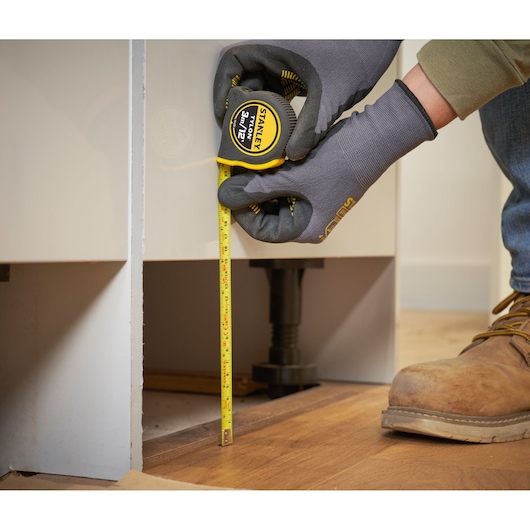 STANLEY 0-30-686 tape measure, yellow, used for vertical measurement against cabinet on wooden floor.