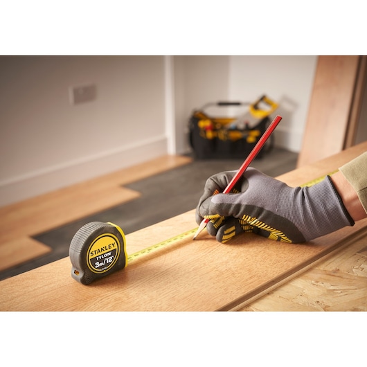 Photo of STANLEY 0-30-686 tape measure in use, person marking wood with pencil while wearing work gloves.