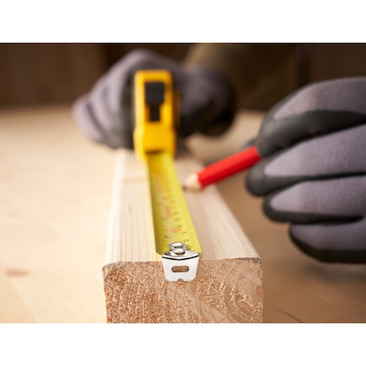 STANLEY 0-30-696 tape measure in use on wood, close-up view with gloves and pencil.