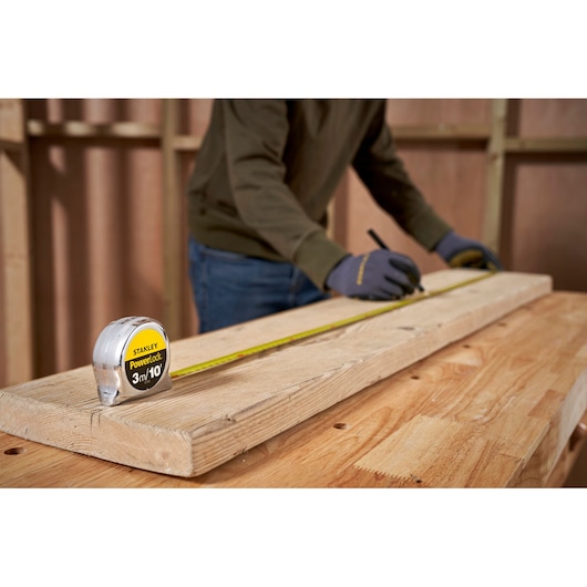 STANLEY 0-33-523 tape measure on wood plank, person marking measurements in workshop setting.