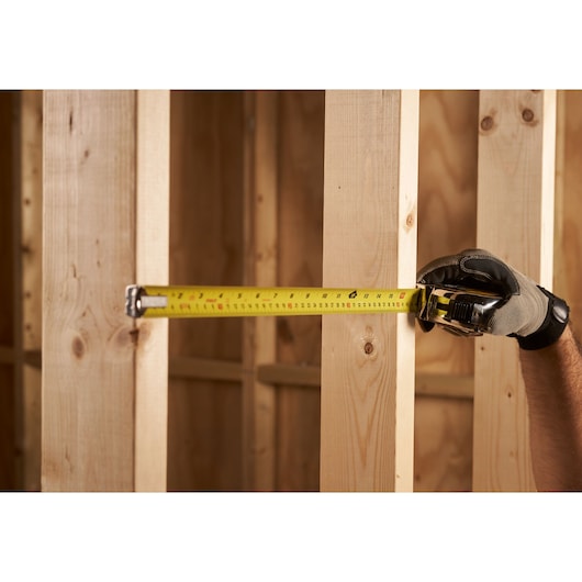 STANLEY 0-33-531 tape measure used on wooden studs, hand wearing glove, close-up photography.