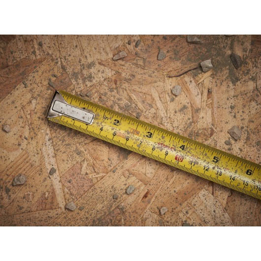 STANLEY 0-33-531 yellow tape measure extended on rough wooden surface with small rocks, product close-up.