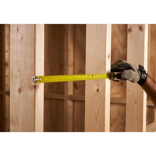 STANLEY 0-33-553 tape measure in use measuring wooden beams, side angle, yellow tape visible.