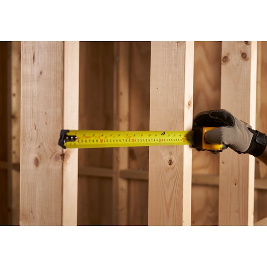 STANLEY 0-33-719 tape measure extended horizontally on wooden studs, side view, worker hand with glove.