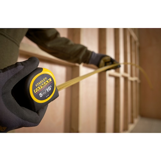 Photo of STANLEY 0-33-719 FATMAX tape measure being used to measure a wooden frame, close-up view.
