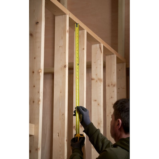 STANLEY 0-33-719 tape measure held vertically against wooden studs, construction setting.