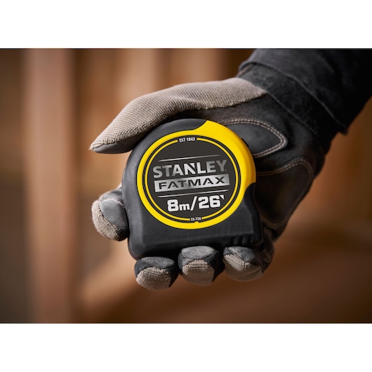 STANLEY 0-33-726 tape measure FATMAX, black and yellow, 8m/26ft, close-up held in a gloved hand.