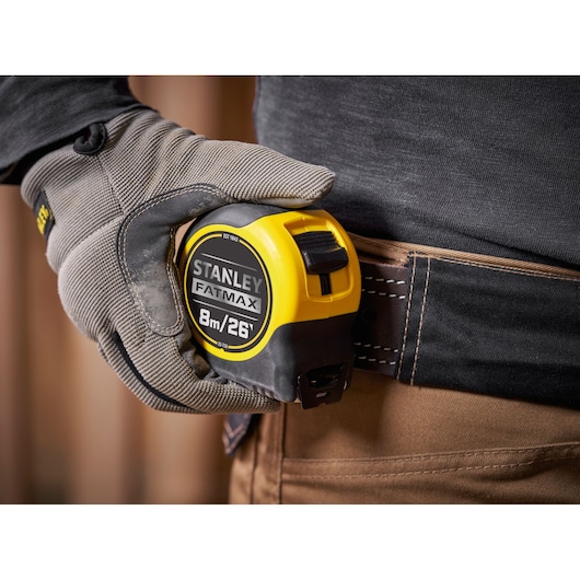Photo of STANLEY 0-33-726 tape measure, yellow and black, clipped to a tool belt, worker wearing gloves.