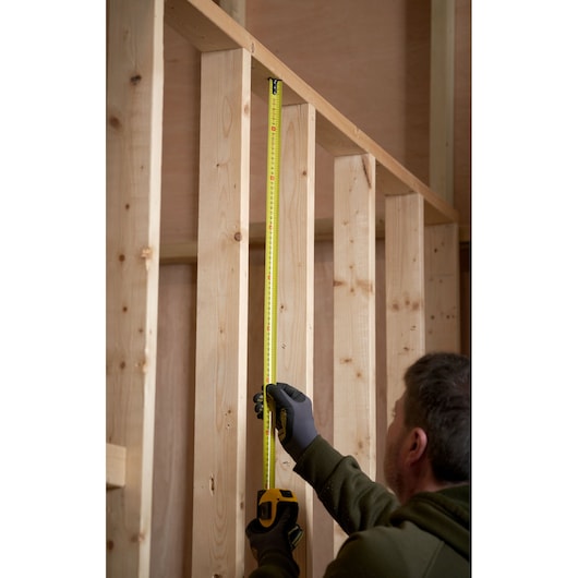 STANLEY 0-33-728 tape measure in use measuring vertical wooden studs, indoor construction setting.