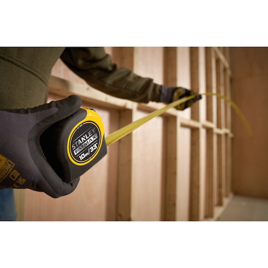 Photo of STANLEY 0-33-805 tape measure held by gloved hand, extended in construction framing setting.
