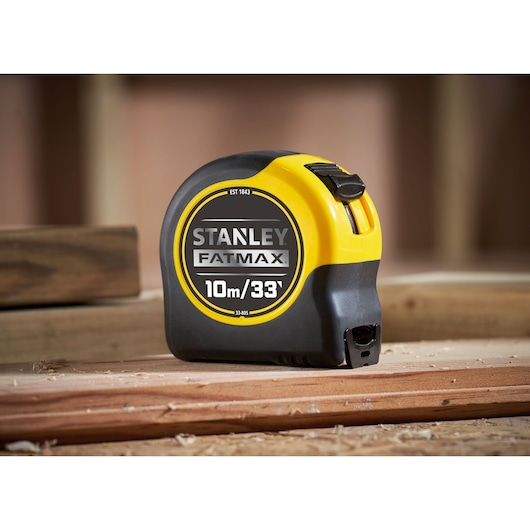 STANLEY 0-33-805 tape measure, FATMAX, 10m/33ft, black and yellow, side angle, on wood surface.