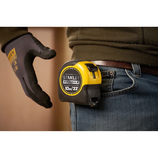 STANLEY 0-33-805 tape measure clipped to jeans, FATMAX branding visible, side view, hand wearing work glove.