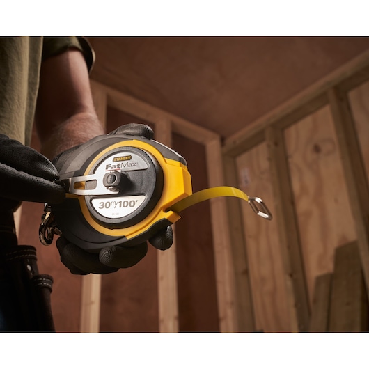 Photo of STANLEY 0-34-132 FatMax 30m/100ft tape measure held by a person wearing gloves.