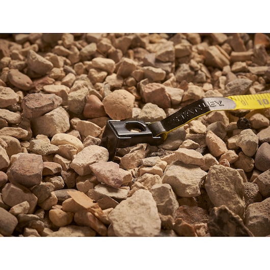 Photo of STANLEY 0-34-262 tape measure end on rocky ground, yellow with black hook, photography category.