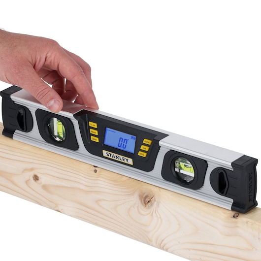 Photo of STANLEY 0-42-063 digital spirit level on wood beam, LCD screen displays 0.0, hand adjusting tool.