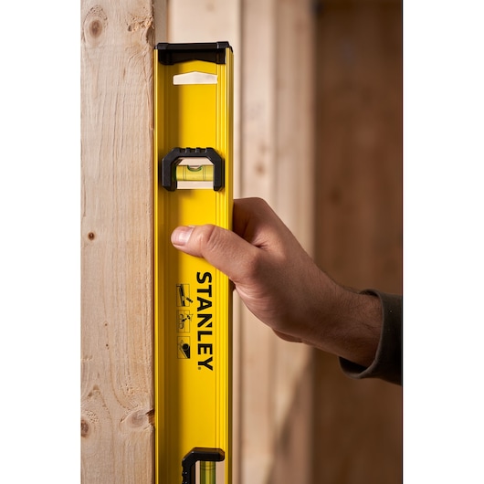 STANLEY 0-42-074 yellow spirit level held vertically against wooden beam, product photography.