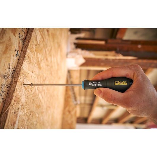 Stanley 0-65-335 hand-held screwdriver driving screw into plywood wall, black and yellow handle.