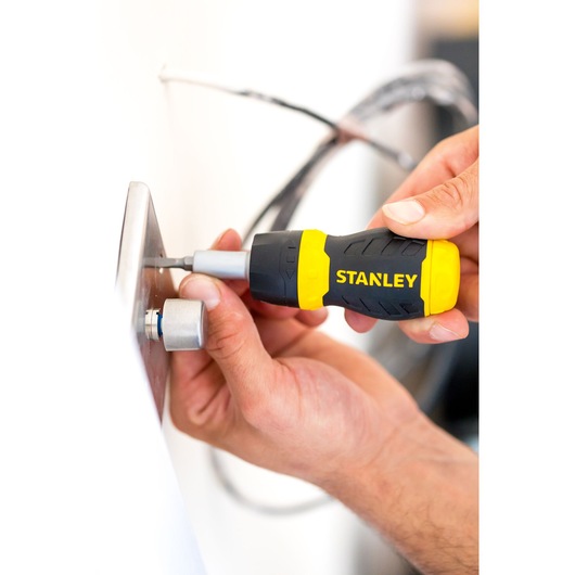 STANLEY 0-66-358 ratcheting screwdriver with yellow and black handle in use tightening a screw.