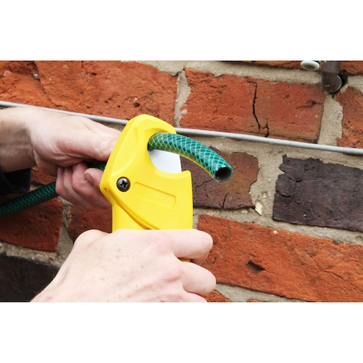 Photo of STANLEY 0-70-450 hose cutter cutting green garden hose against brick wall.