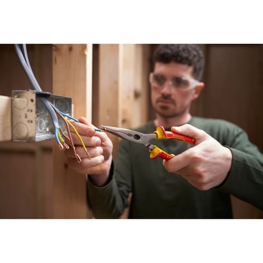 Photo of STANLEY 0-84-007 insulated pliers gripping electrical wire near metal junction box during installation.
