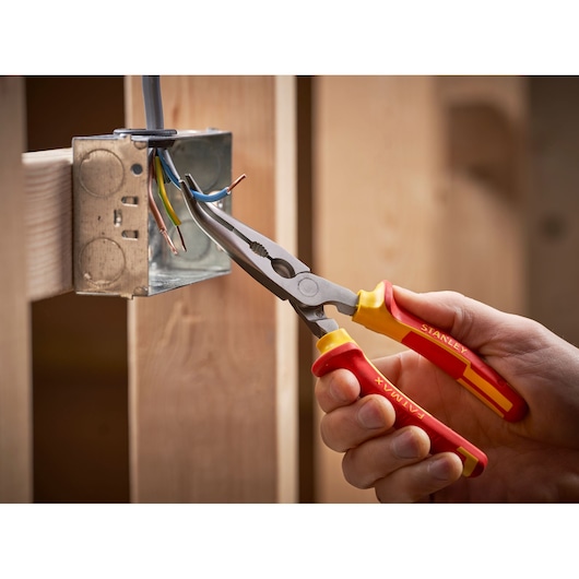 STANLEY 0-84-008 insulated long nose pliers in use, gripping electrical wire near metal junction box.