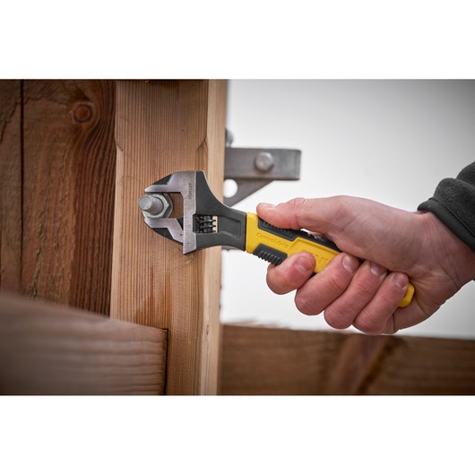 STANLEY 0-90-948 adjustable wrench with yellow and black handle used to tighten bolt on wooden structure.