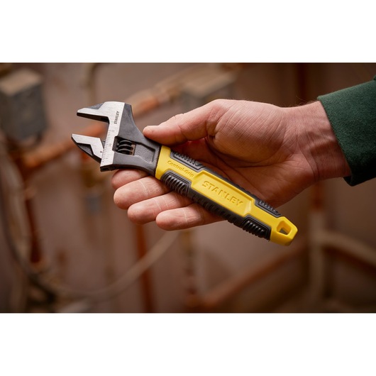 STANLEY 0-90-949 adjustable wrench with yellow and black handle, held in hand, plumbing background.
