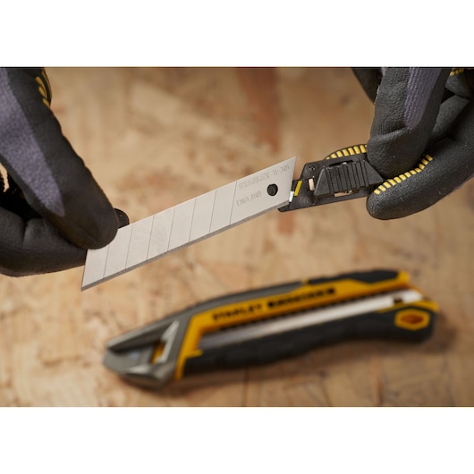 STANLEY 1-11-301 utility knife blade close-up, held by gloved hands, cutter on wood background.