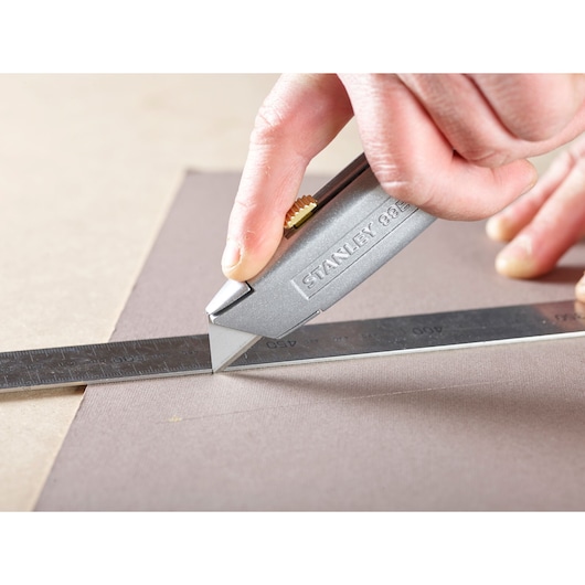 Photo of STANLEY 1-11-911 utility knife cutting material with a metal ruler for alignment.
