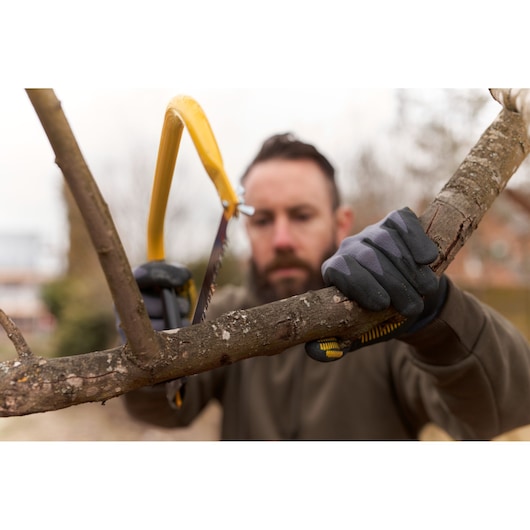 STANLEY 1-20-447 hand saw with yellow frame cutting tree branch outdoors, person wearing work gloves.