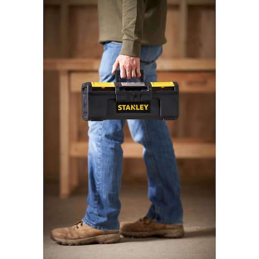 Photo of STANLEY 1-79-216 black tool box with yellow accents carried by person in work boots.