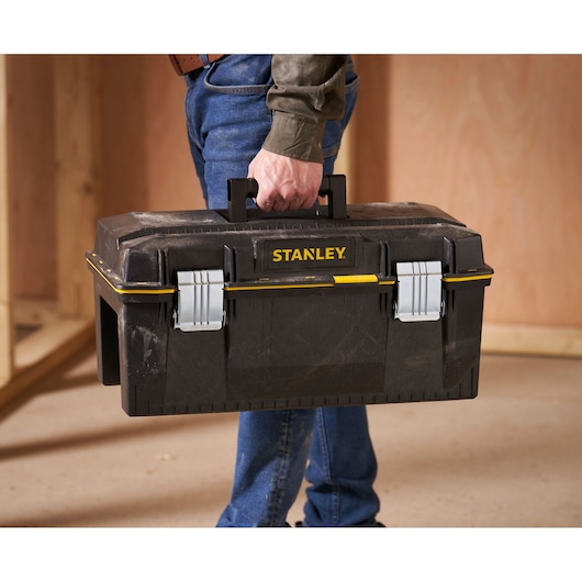 Stanley 1-94-749 toolbox with metal latches, carried by hand in workshop setting.