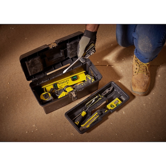 STANLEY 1-94-857 tool box opened with assorted hand tools and yellow level on indoor floor.