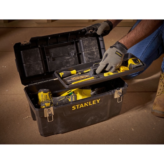 STANLEY 1-94-858 toolbox with yellow hand tools, open on floor, person wearing gloves lifts tray.