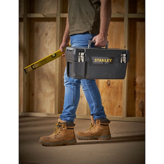 Photo of STANLEY 1-94-858 toolbox and level, carried by a person wearing work boots, shown in a construction setting.