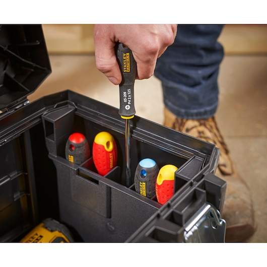 A close-up of a person taking a STANLEY screwdriver from a black tool box with several other screwdrivers inside, showing the tool organization and easy access.