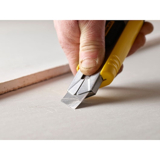 Photo of STANLEY 2-11-725 utility knife cutting drywall sheet close-up, showing yellow handle and metal blade.