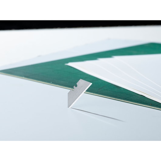 STANLEY 2-11-911 utility blade upright on white surface, green cutting mat and papers in background.