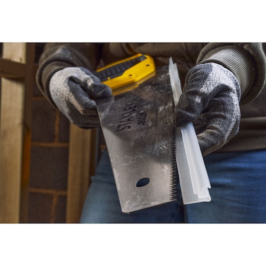 Photo of STANLEY 2-15-288 hand saw held by gloved hands, close-up showing blade and teeth.